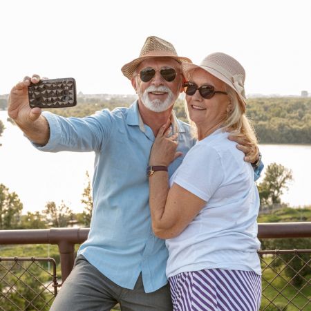 The Lodges of Huntersville An elderly couple happily posing for a selfie with a smartphone, showcasing their affection and connection.