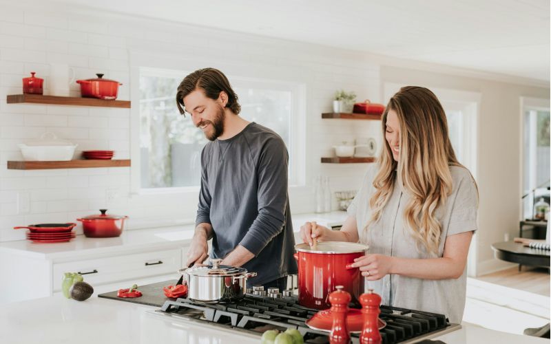 The Lodge of Huntersville. A man and woman cooking together in a kitchen surrounded by pots and pans on the stove and countertops.