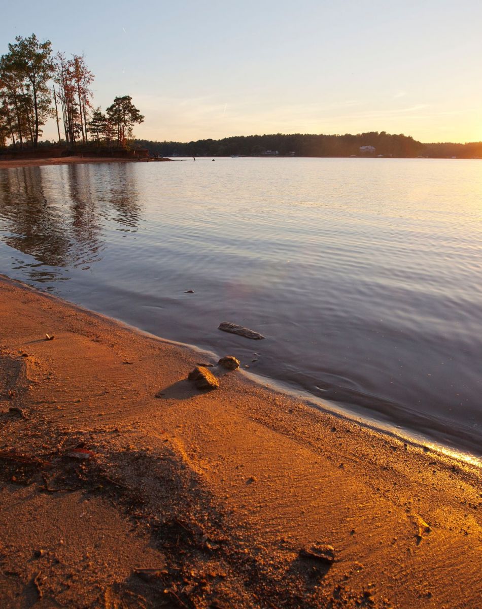 The Lodges of Huntersville A picturesque beach scene featuring soft sand and a vibrant sunset over the tranquil ocean.
