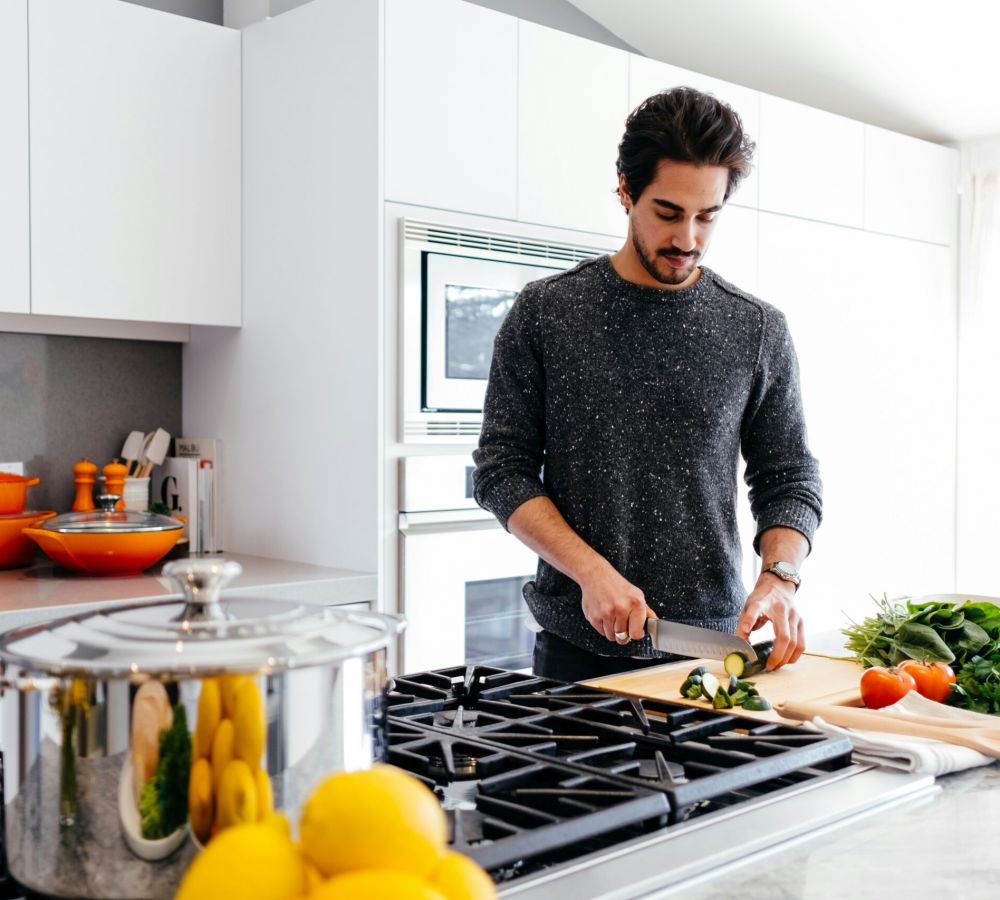The Lodges of Huntersville A man is chopping vegetables on a kitchen counter, surrounded by various fresh produce and kitchen utensils.