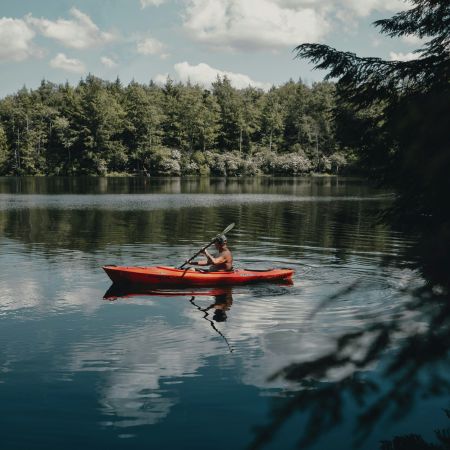 The Lodges of Huntersville A man paddles a red canoe across a serene lake surrounded by trees and mountains in the background.