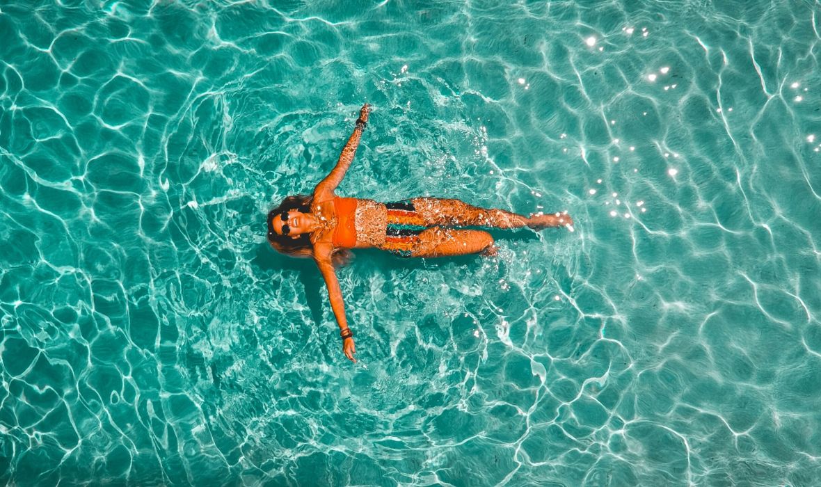 The Lodges of Huntersville A woman peacefully floating on her back in calm water, surrounded by a serene natural landscape.