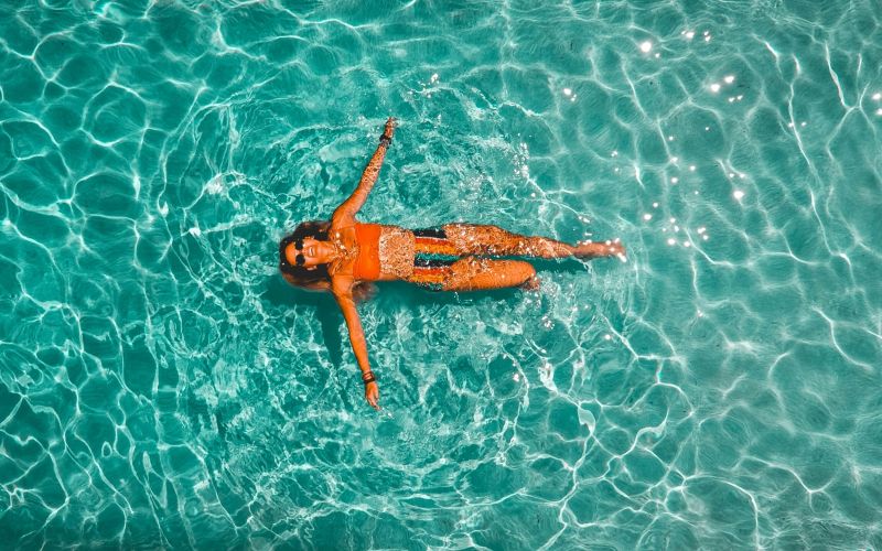 The Lodges of Huntersville A woman peacefully floating on her back in calm water, surrounded by a serene natural landscape.