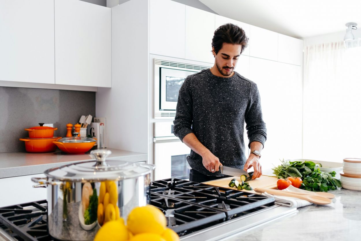 The Lodges of Huntersville A man is chopping vegetables on a kitchen counter, surrounded by various fresh produce and kitchen utensils.