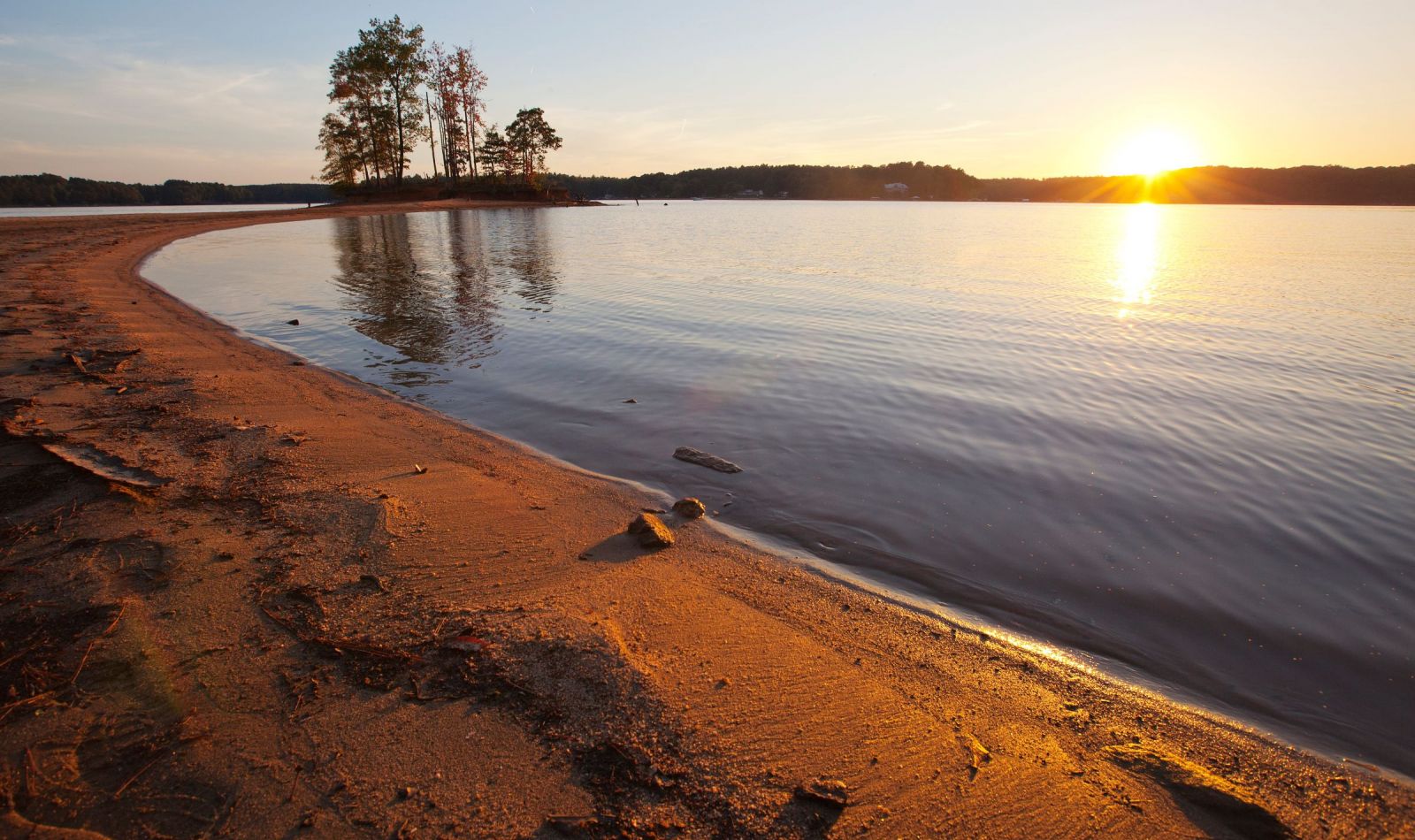 The Lodges of Huntersville A picturesque beach scene featuring soft sand and a vibrant sunset over the tranquil ocean.