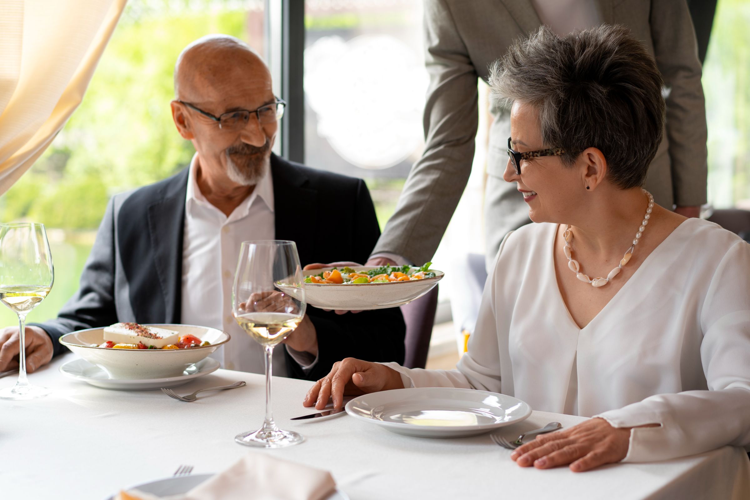 The Lodges of Huntersville A man presents a plate of food to a woman, highlighting a warm interaction during a meal.