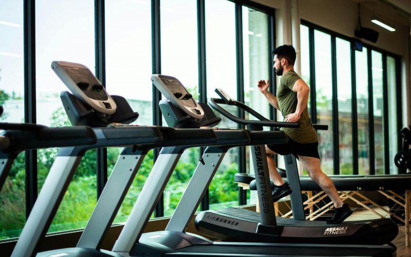 The Lodges of Huntersville A man running on a treadmill in a gym, focused on his workout amidst various gym equipment in the background.