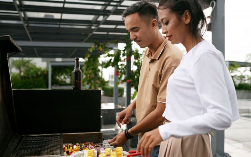 The Lodges of Huntersville A man and woman are grilling food together outdoors, enjoying a sunny day and preparing a meal.