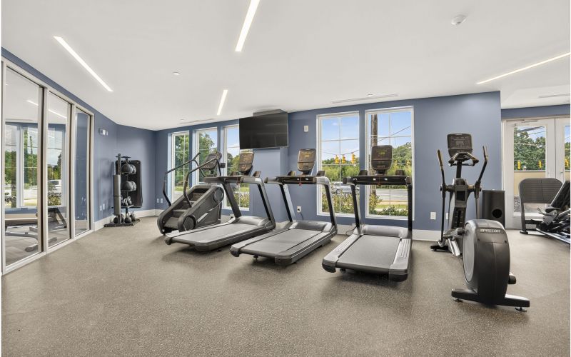 The Lodges of Huntersville A man running on a treadmill in a gym, focused on his workout amidst various gym equipment in the background.