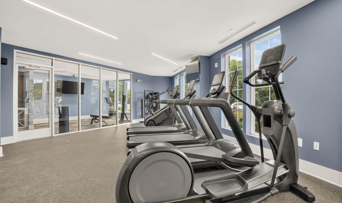 The Lodges of Huntersville A man squats with a barbell on his shoulders, focusing on his form in a gym setting.