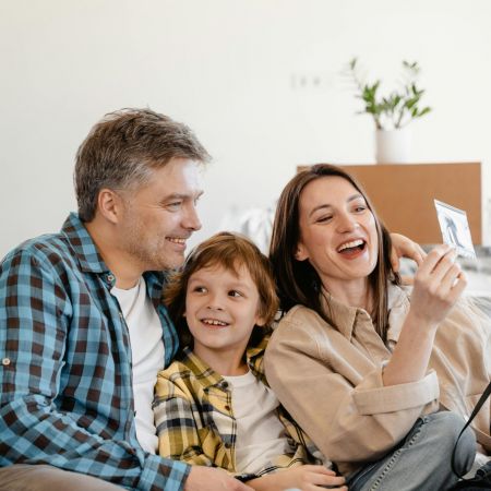 The Lodges of Huntersville A family of four sits together on a couch, one member holding a cell phone while they engage in conversation.