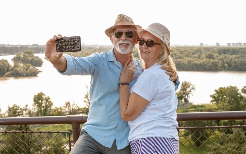 The Lodges of Huntersville An elderly couple happily posing for a selfie with a smartphone, showcasing their affection and connection.